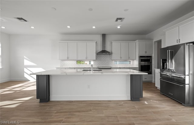 kitchen with a center island with sink, appliances with stainless steel finishes, backsplash, and wall chimney exhaust hood