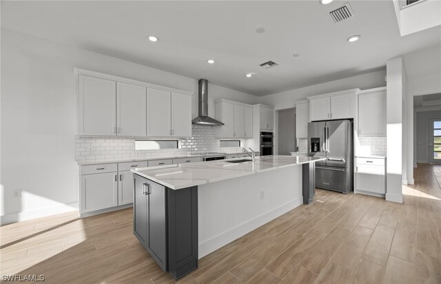 kitchen with appliances with stainless steel finishes, backsplash, wall chimney range hood, an island with sink, and sink