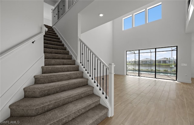 stairway with a water view, wood-type flooring, and a towering ceiling