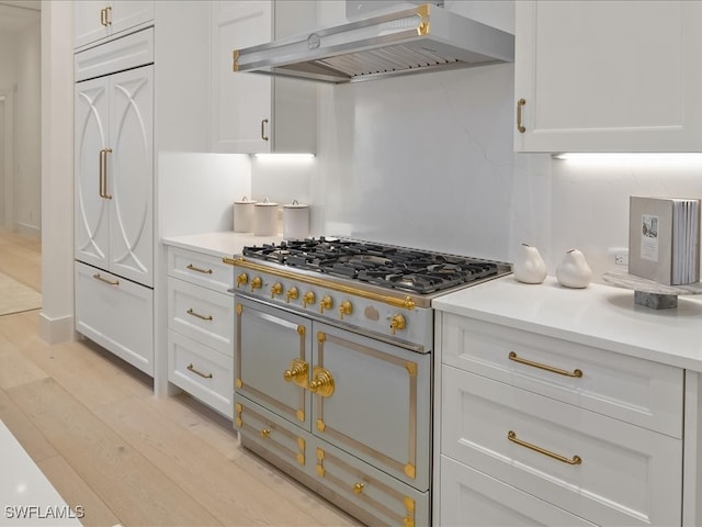 kitchen featuring backsplash, premium range, light hardwood / wood-style flooring, wall chimney exhaust hood, and white cabinetry