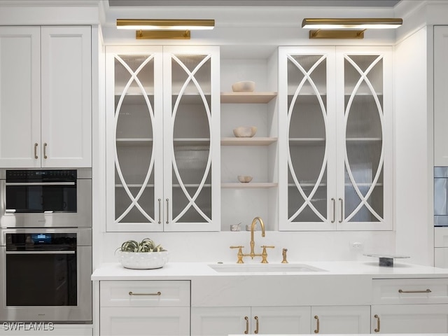 bar with stainless steel double oven, white cabinetry, and sink