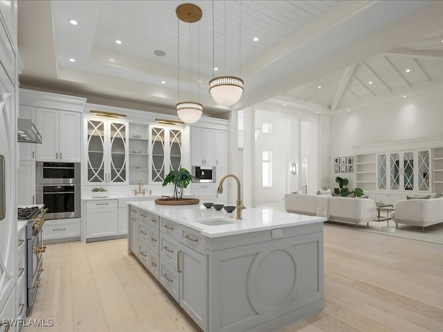 kitchen with appliances with stainless steel finishes, light wood-type flooring, sink, hanging light fixtures, and an island with sink