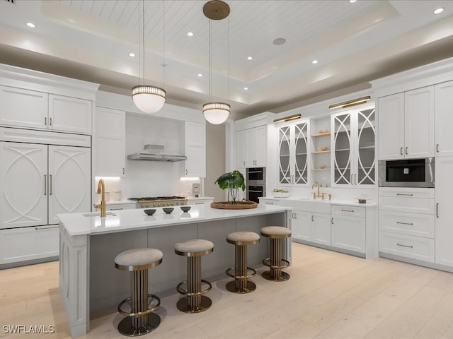 kitchen featuring a raised ceiling, a center island with sink, white cabinets, and decorative light fixtures