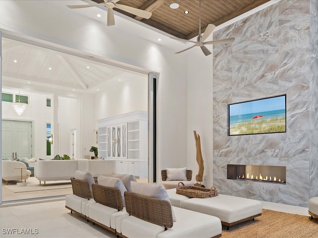 living room with ceiling fan, wooden ceiling, a premium fireplace, beamed ceiling, and a towering ceiling