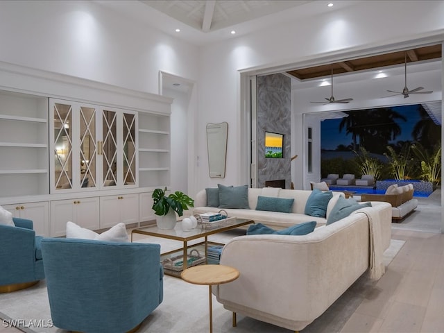 living room with built in shelves, ceiling fan, a high ceiling, light hardwood / wood-style floors, and a fireplace