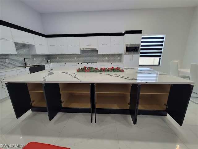 kitchen with light stone counters, white cabinetry, a kitchen island, tasteful backsplash, and stainless steel microwave