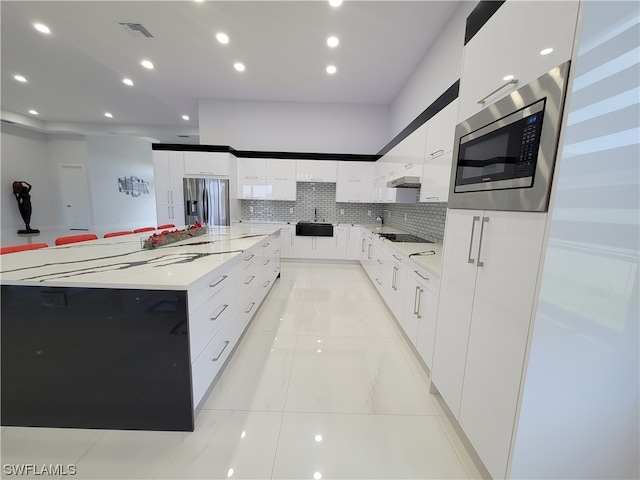 kitchen featuring white cabinetry, a spacious island, backsplash, stainless steel appliances, and sink