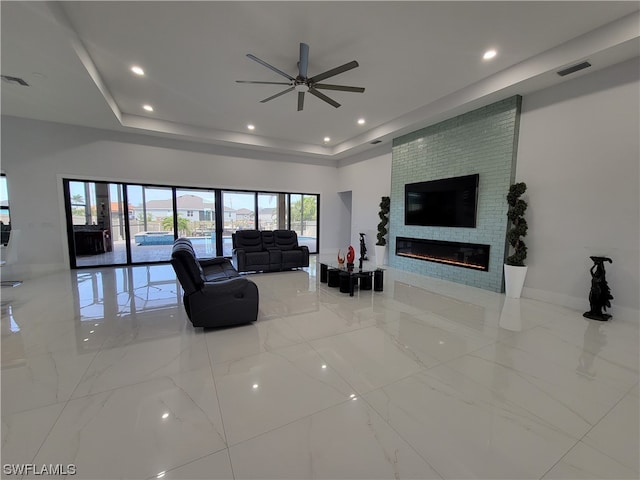 living room with ceiling fan, a tray ceiling, and a fireplace