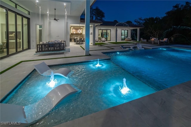pool at night featuring a patio, an outdoor hangout area, pool water feature, and ceiling fan