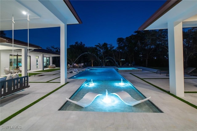 pool at night featuring a patio and pool water feature