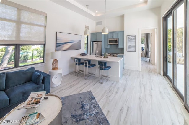 living room with a towering ceiling, a raised ceiling, sink, and a wealth of natural light