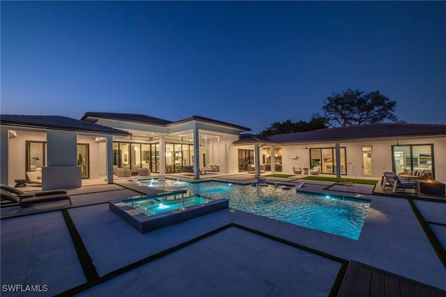 pool at dusk featuring an in ground hot tub, an outdoor hangout area, and a patio area