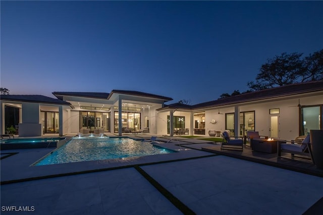 pool at dusk with pool water feature, a patio area, and an outdoor fire pit