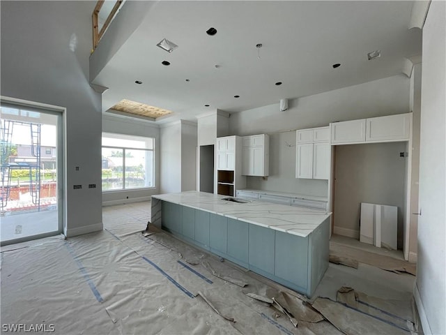 kitchen featuring a spacious island, sink, light stone counters, and white cabinets