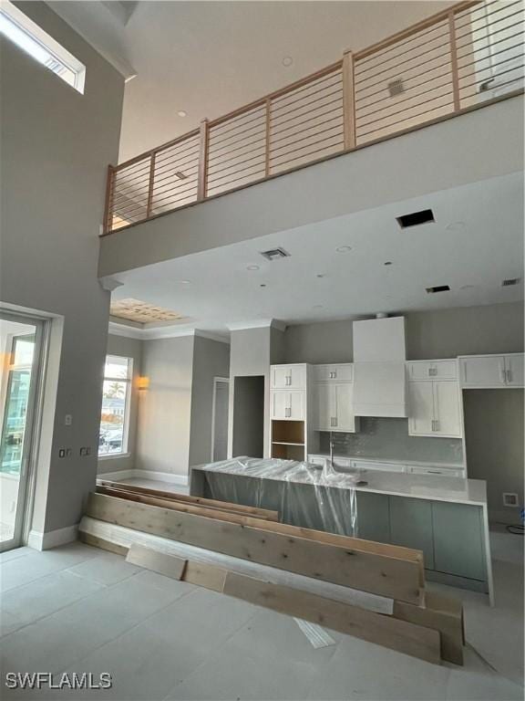 kitchen featuring backsplash, white cabinets, crown molding, a towering ceiling, and custom range hood