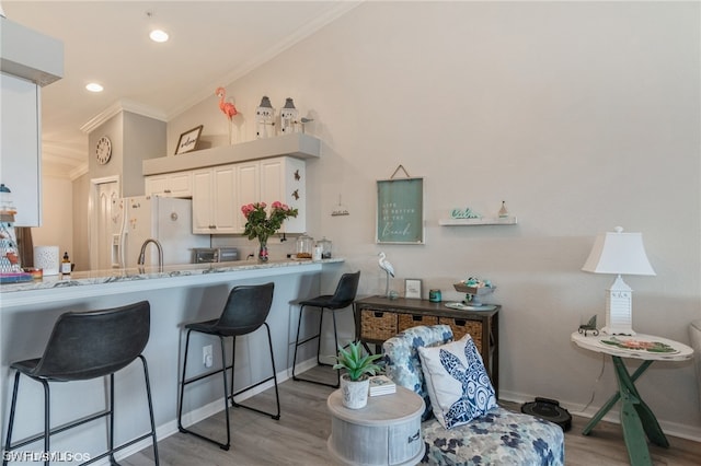 kitchen with light wood-type flooring, white cabinets, white refrigerator, a breakfast bar area, and ornamental molding