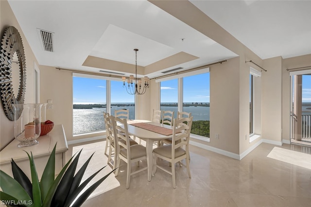 dining space with a raised ceiling, a water view, and an inviting chandelier