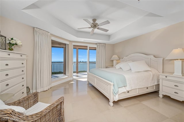 bedroom with access to exterior, a raised ceiling, ceiling fan, and a water view