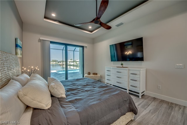 bedroom with light hardwood / wood-style floors, access to outside, ceiling fan, and a raised ceiling