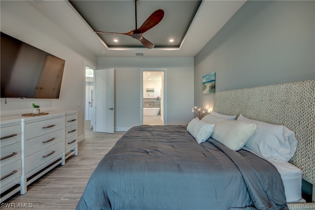 bedroom featuring connected bathroom, ceiling fan, a tray ceiling, and light hardwood / wood-style flooring