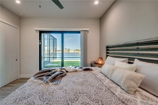 bedroom with access to outside, light hardwood / wood-style flooring, ceiling fan, and a water view