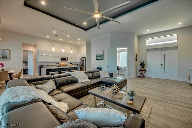 living room with light hardwood / wood-style floors, ceiling fan, a tray ceiling, and a high ceiling