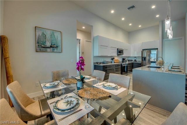 dining area featuring a high ceiling, sink, and light wood-type flooring