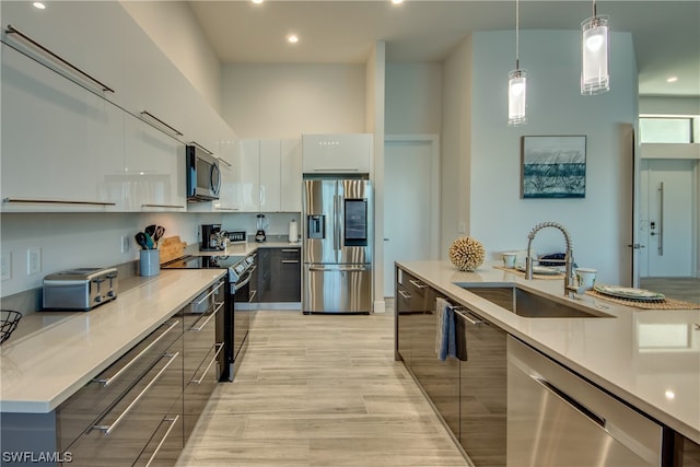 kitchen with a high ceiling, appliances with stainless steel finishes, white cabinetry, hanging light fixtures, and light wood-type flooring