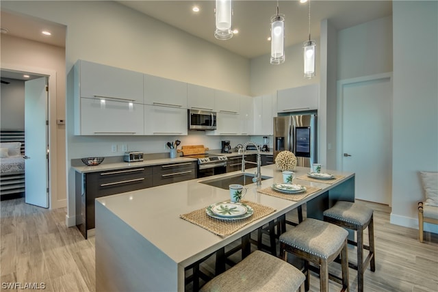 kitchen with a kitchen bar, hanging light fixtures, light hardwood / wood-style flooring, and stainless steel appliances