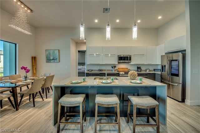 kitchen with a towering ceiling, stainless steel appliances, an inviting chandelier, decorative light fixtures, and light wood-type flooring