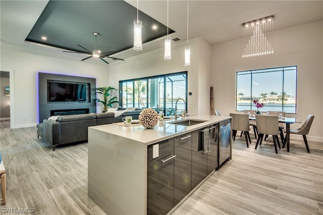 kitchen featuring pendant lighting, a tray ceiling, a center island with sink, and light wood-type flooring