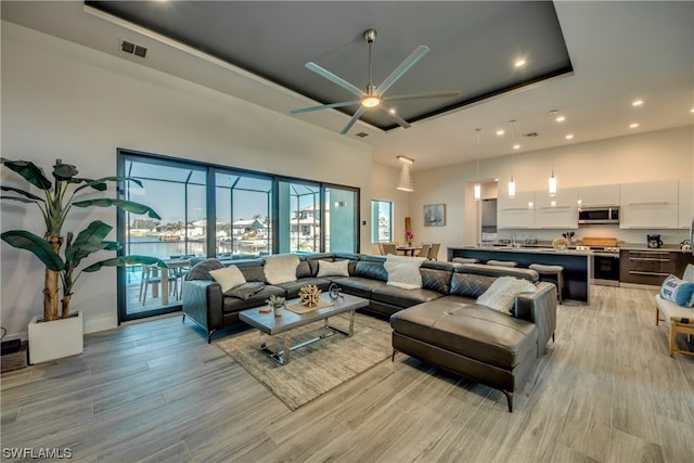 living room featuring light hardwood / wood-style floors, ceiling fan, and a tray ceiling