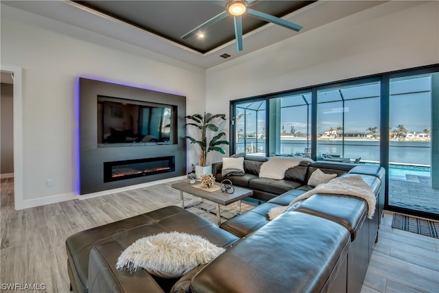 living room featuring a water view, a tray ceiling, ceiling fan, and light hardwood / wood-style flooring