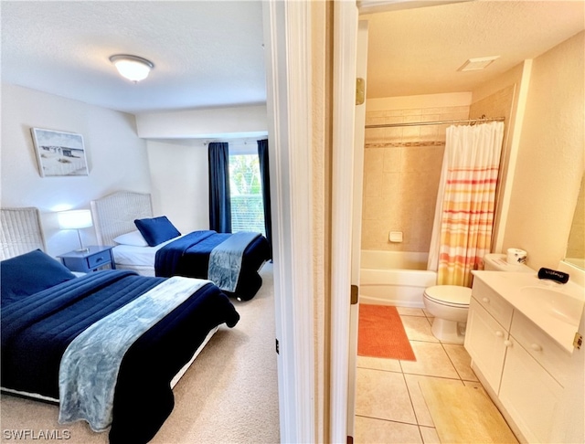 bedroom with a textured ceiling, ensuite bathroom, light tile floors, and sink