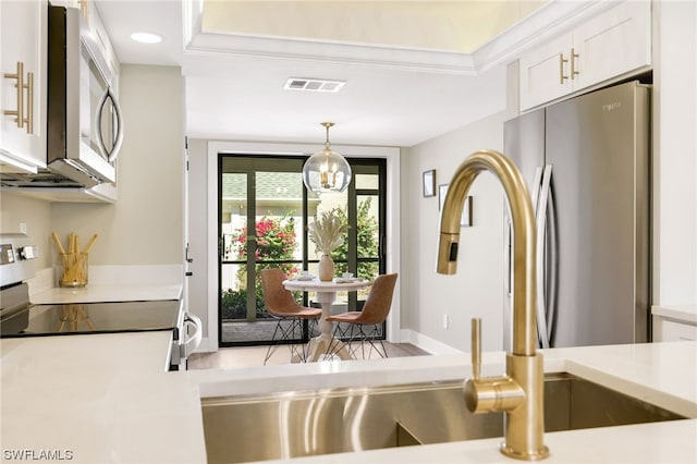 kitchen featuring pendant lighting, stainless steel appliances, a tray ceiling, an inviting chandelier, and white cabinetry