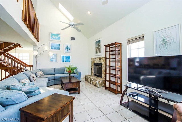 tiled living room with ceiling fan, a stone fireplace, and high vaulted ceiling