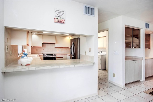 kitchen with light tile floors, kitchen peninsula, washer / clothes dryer, appliances with stainless steel finishes, and backsplash