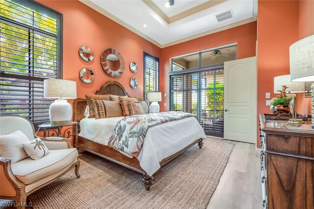 bedroom with ornamental molding, access to exterior, light hardwood / wood-style floors, and a tray ceiling