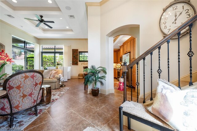 foyer with dark tile patterned flooring, ornamental molding, a raised ceiling, and ceiling fan