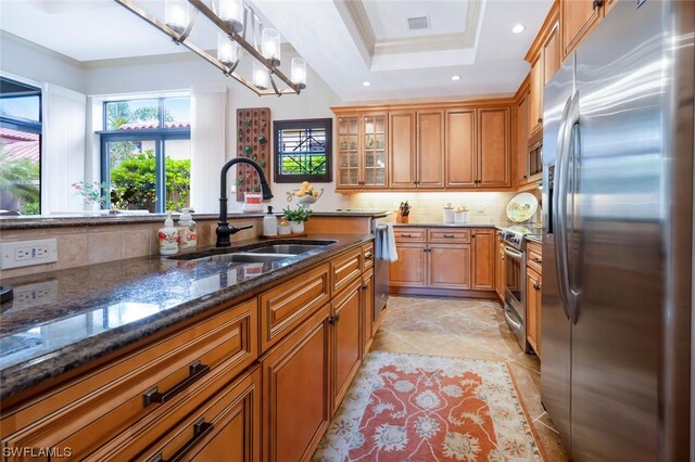 kitchen with appliances with stainless steel finishes, sink, dark stone countertops, hanging light fixtures, and crown molding