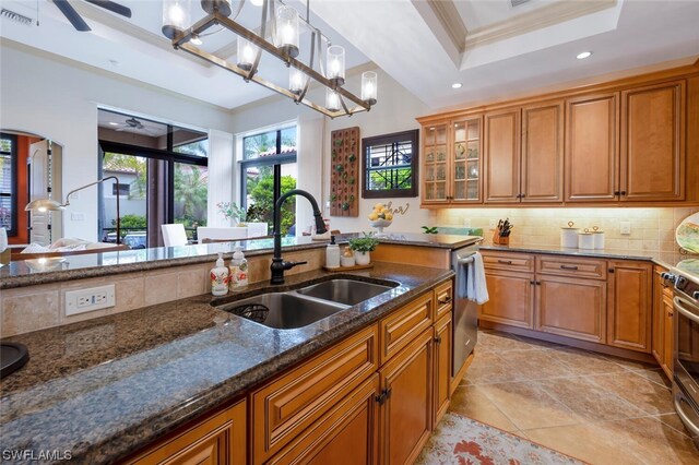 kitchen featuring sink, hanging light fixtures, ornamental molding, a raised ceiling, and dark stone counters