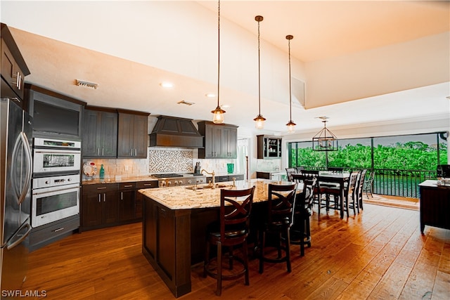 kitchen with premium range hood, decorative light fixtures, appliances with stainless steel finishes, light stone counters, and dark hardwood / wood-style flooring