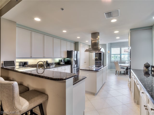 kitchen featuring a kitchen island, white cabinetry, dark stone counters, island exhaust hood, and stainless steel refrigerator with ice dispenser