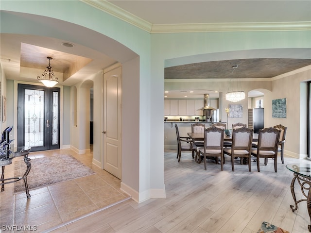 foyer with crown molding, an inviting chandelier, light hardwood / wood-style floors, and a tray ceiling