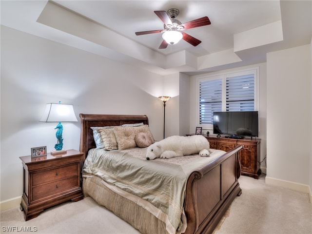 bedroom with light carpet, a tray ceiling, and ceiling fan