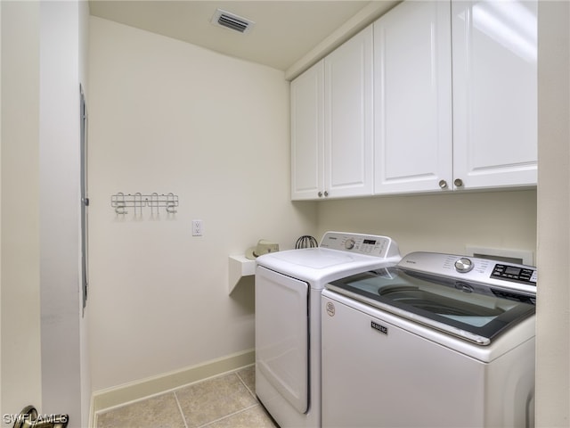 clothes washing area featuring washing machine and dryer, cabinets, and light tile patterned flooring