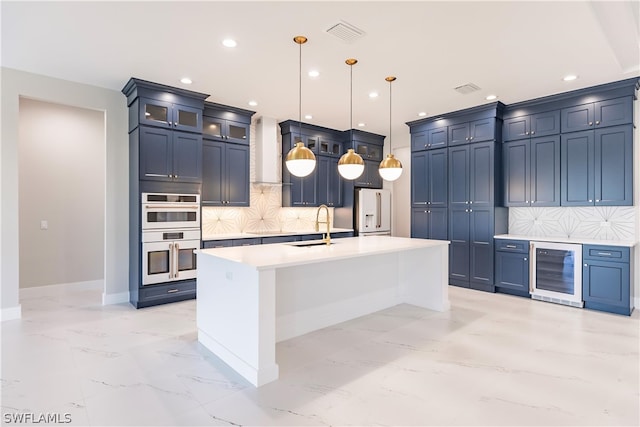 kitchen featuring an island with sink, stainless steel double oven, beverage cooler, backsplash, and blue cabinets