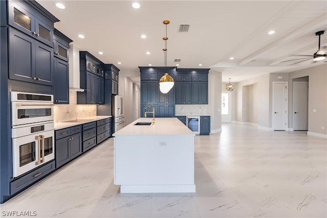 kitchen with an island with sink, light tile floors, tasteful backsplash, and double oven