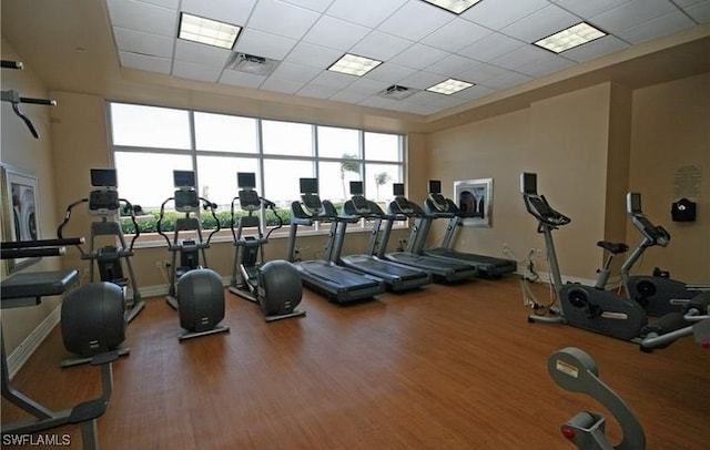 exercise room with hardwood / wood-style flooring, a towering ceiling, and a drop ceiling