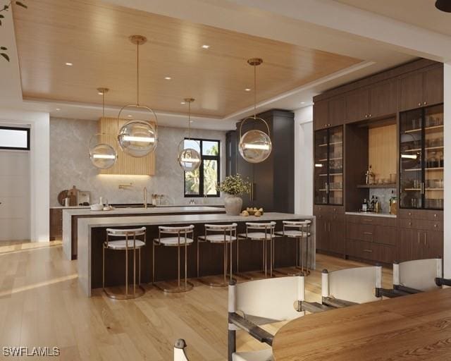 bar with light hardwood / wood-style flooring, dark brown cabinetry, decorative light fixtures, and a raised ceiling